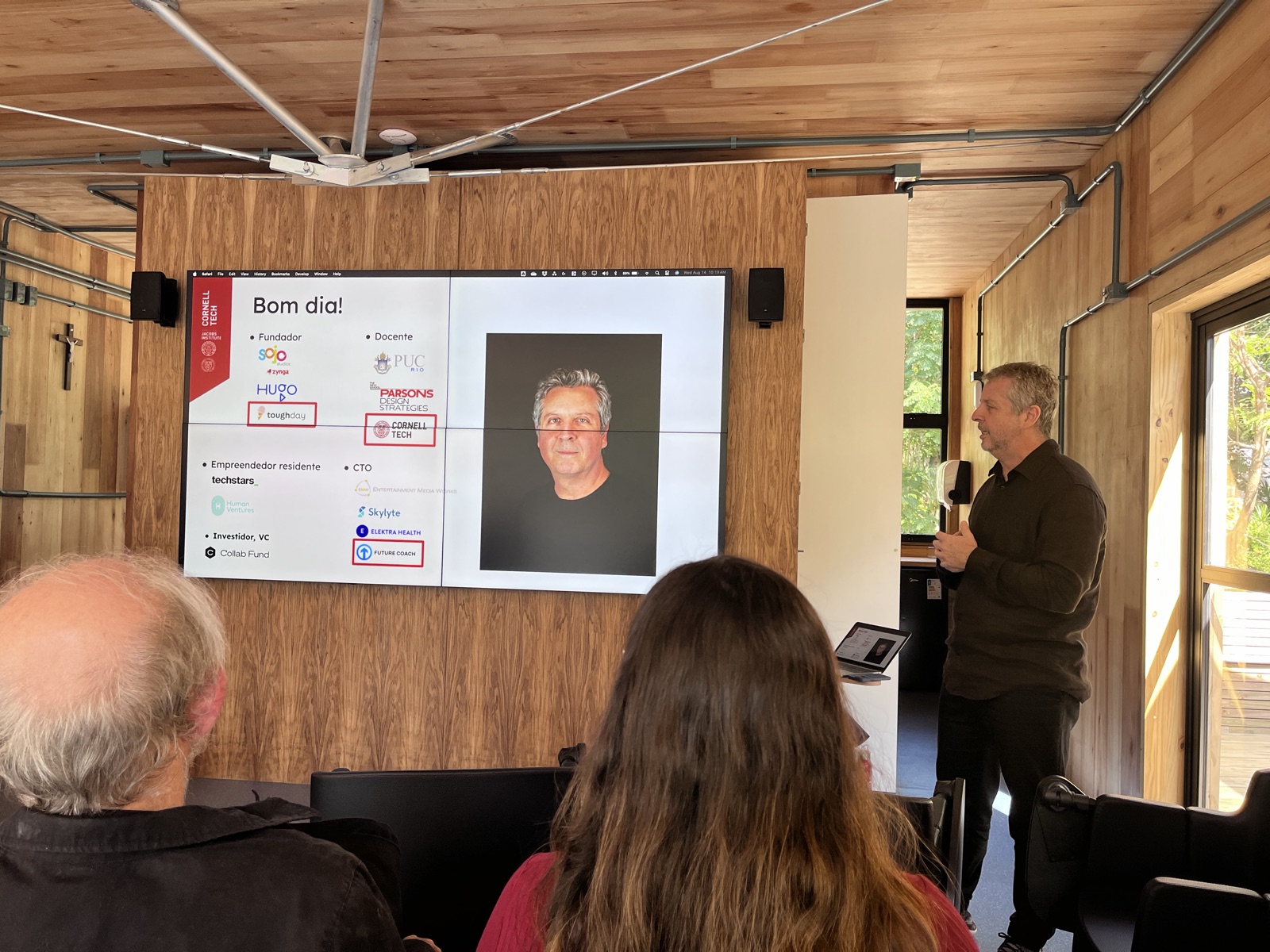 Alberto giving a talk in Portuguese at Cornell Tech's Jacobs Institute, next to a bilingual slide summarizing his roles as founder, professor, EIR, and CTO
